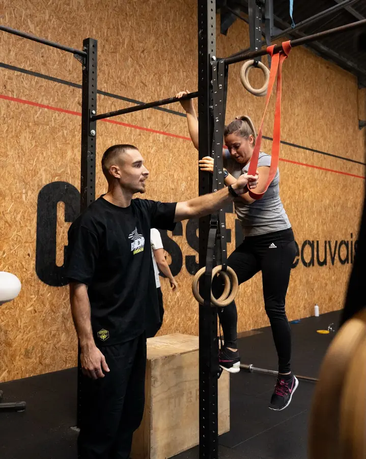 Un coach accompagne une adhérente pendant un exercice aux anneaux